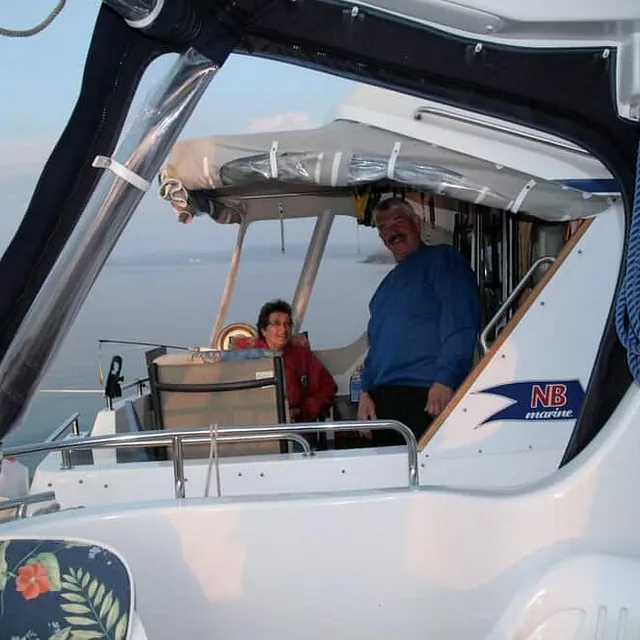 Person sitter i båt med kalesje ved brygge i småbåthavn.