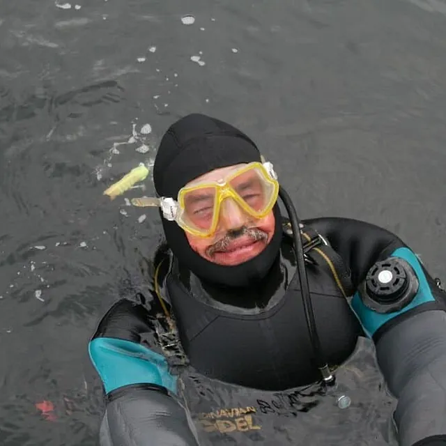 Dykker i tørrdrakt og maske flyter i sjøen.