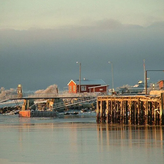 Vinterlig brygge med rim og liten rød bygning ved stille sjø.