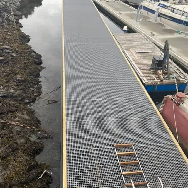 Flytebrygge med metallristdekke langs svaberg og fortøyde båter.