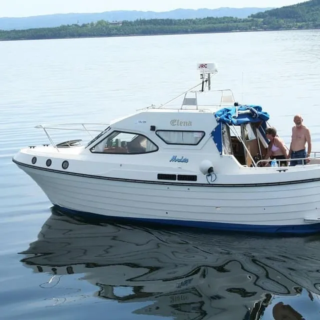 Motorbåt med to personer om bord på stille fjord.