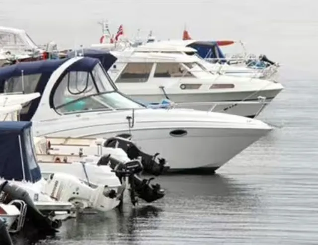 Rekke av motorbåter fortøyd side om side i småbåthavn.