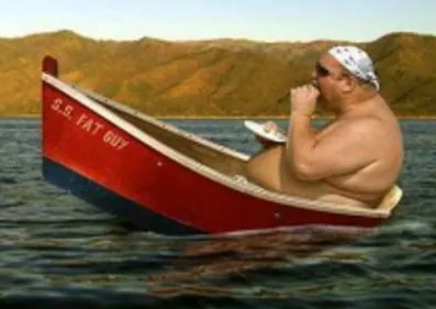 Kraftig mann sitter i liten rød robåt på stille vann med fjell i bakgrunnen.