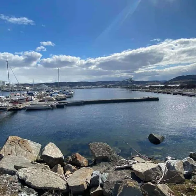 Småbåthavn sett fra land med steiner i forgrunnen og sol over fjorden.