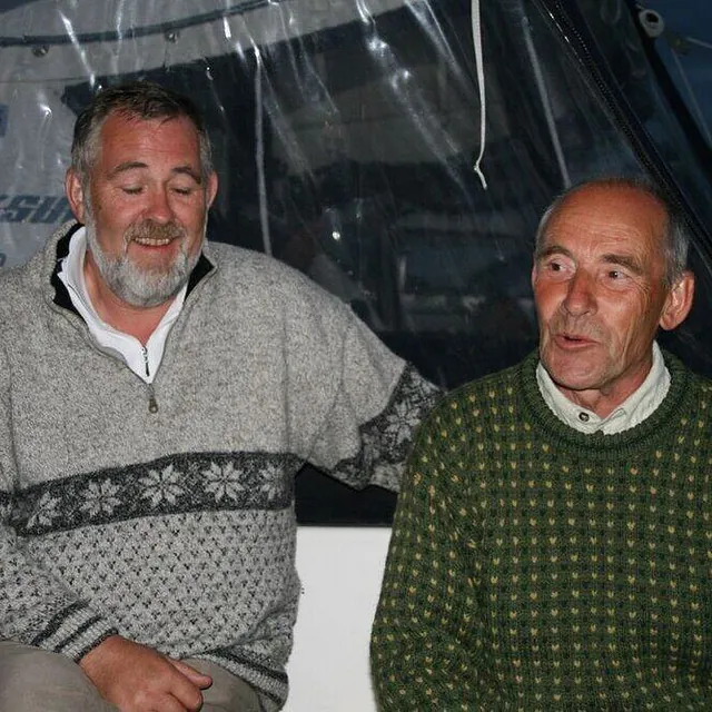 To voksne menn i strikkegensere sitter sammen og prater om bord i en båt.