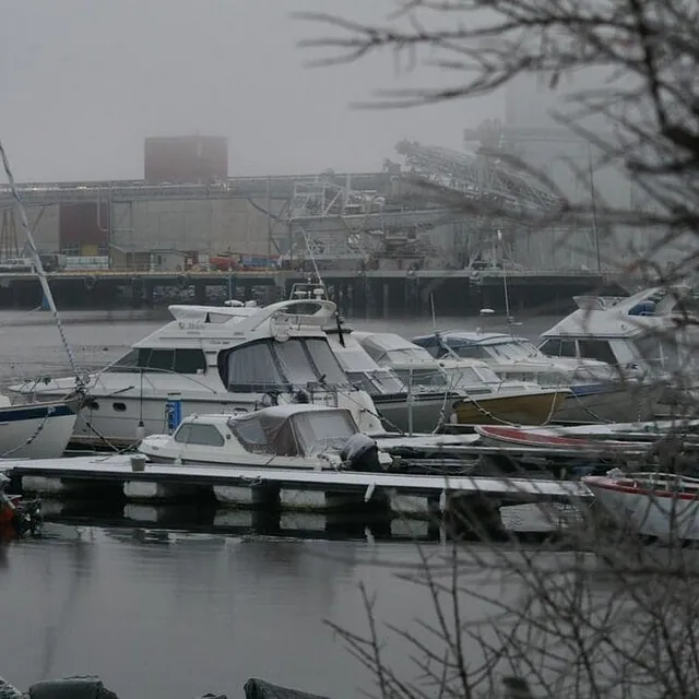 Småbåthavn med motorbåter ved brygge under grå og tåkete himmel.