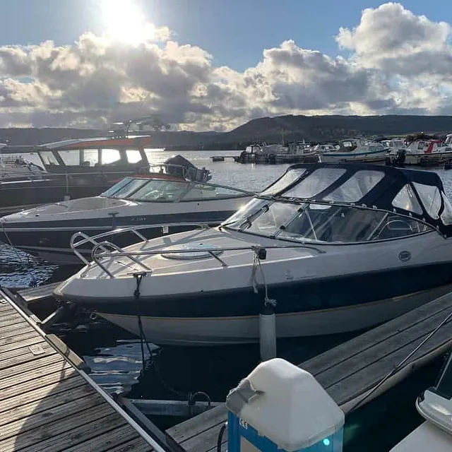 Fritidsbåter fortøyd langs brygge i solskinn med fjell i bakgrunnen.