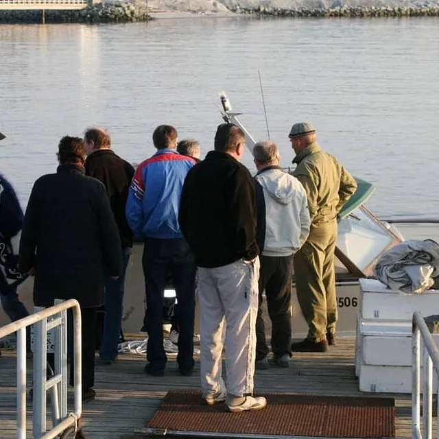 Gruppe menn samlet på brygge rundt liten båt.