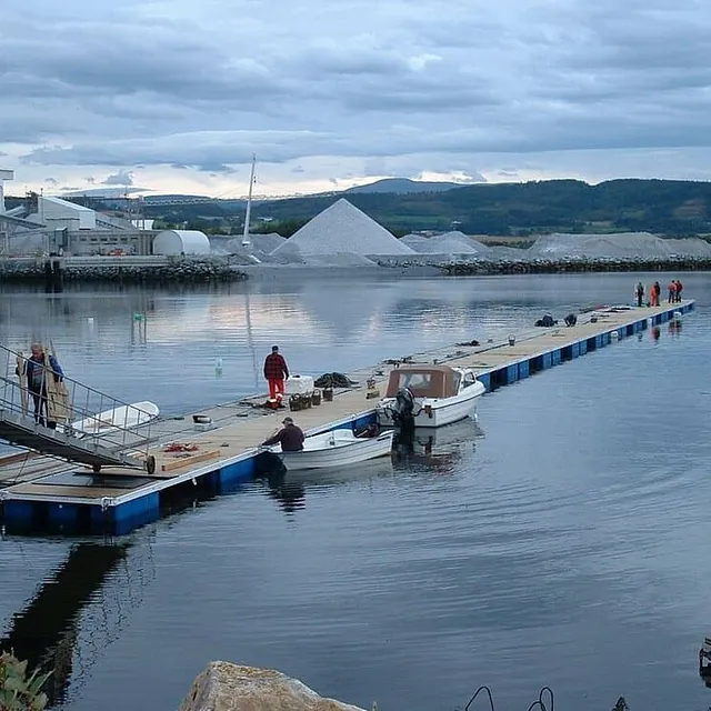 Personer arbeider på lang flytebrygge med båter i rolig havn.