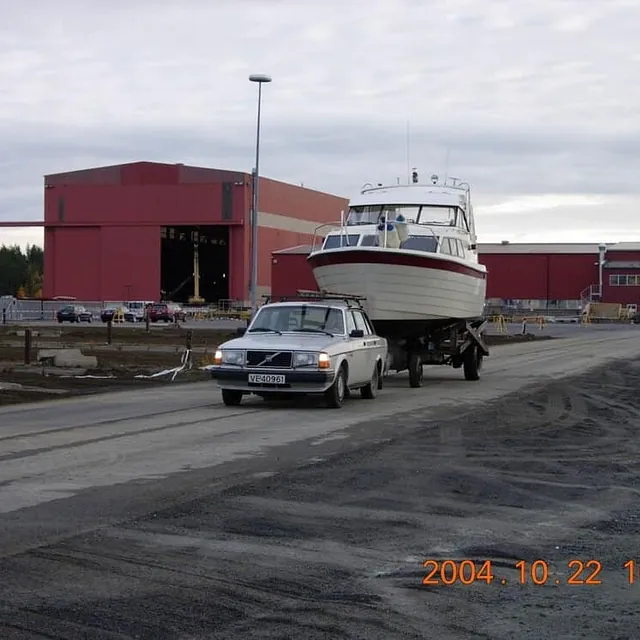 Personbil trekker fritidsbåt på henger gjennom industriområde.