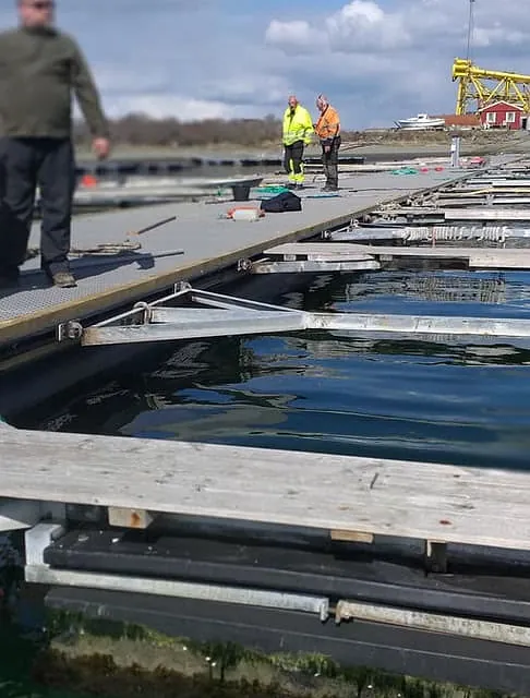 To arbeidere står på flytebrygge under montering i havn.