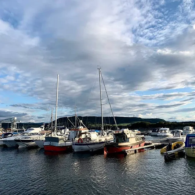 Småbåthavn med seilbåter og motorbåter under delvis skyet himmel.