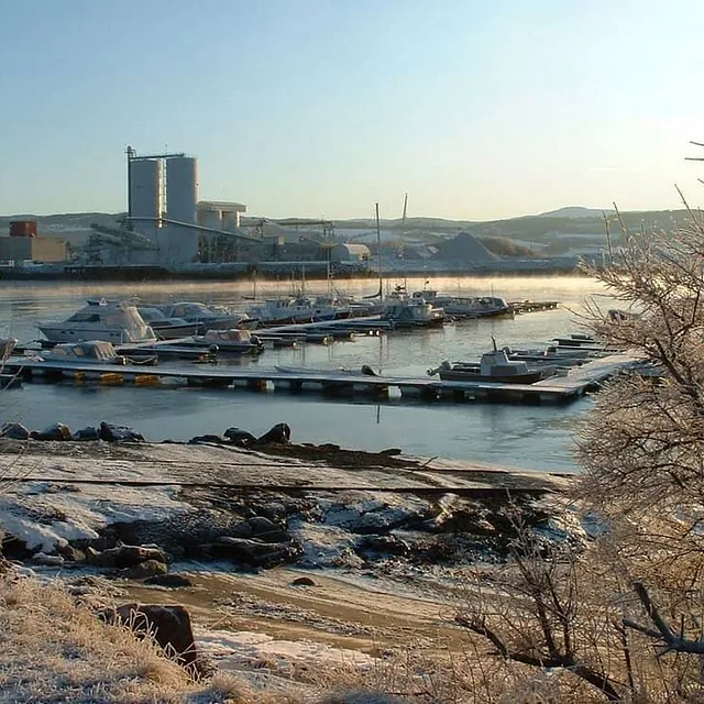 Vinterstemning i småbåthavn med rim på bakken og industriområde i bakgrunnen.