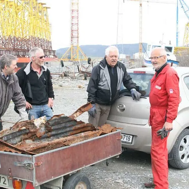 Fire menn laster rustent metallskrap på tilhenger ved industrihavn.