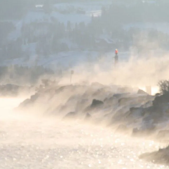 Sjørøyk og tåke stiger opp fra vannet ved en steinmolo i et vinterlandskap.