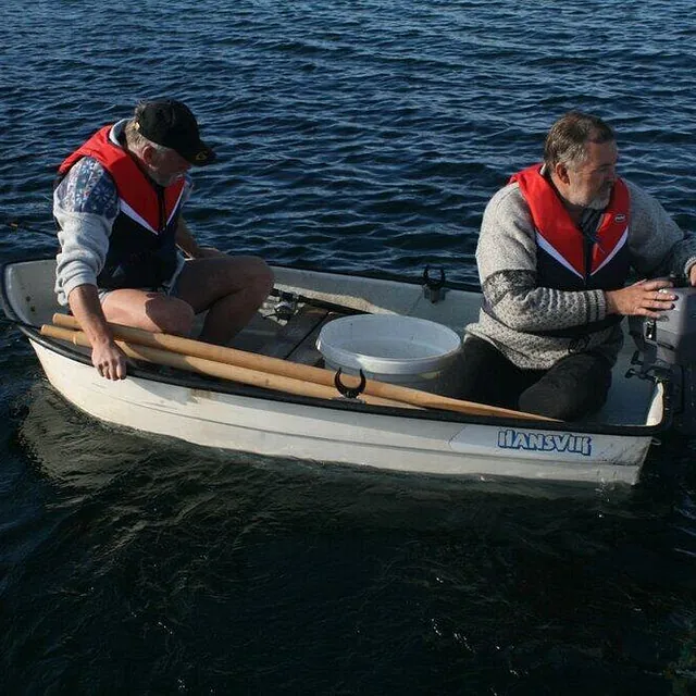 To menn i robåt med påhengsmotor og redningsvester på sjøen.
