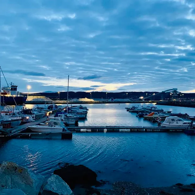 Småbåthavn i kveldslys med opplyste lamper og båter ved brygge.