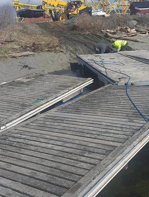 Arbeidere monterer flytebrygger med hjullaster og kraner i bakgrunnen.