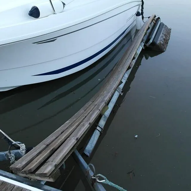 Motorbåt fortøyd ved flytebrygge med treplanker og stille vann rundt.