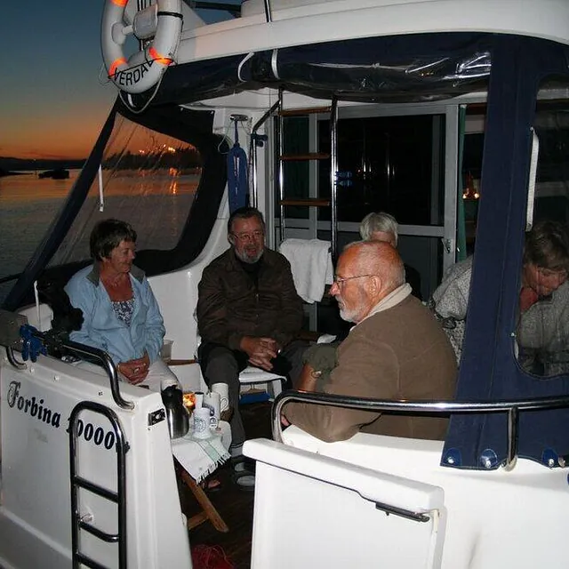 Fire personer sitter samlet til hyggelig lag under kalesjen på akterdekket av en hvit båt.