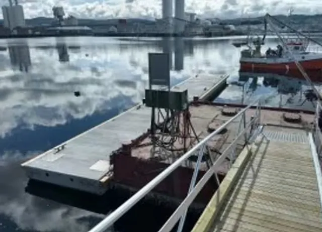 Flytebrygge med landgang og arbeidsutstyr ved kai i rolig havn.