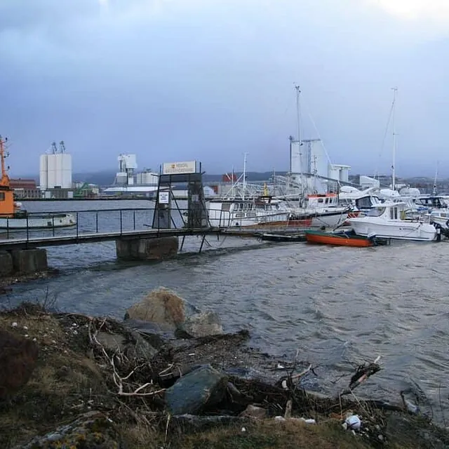 En gangbro fører ut til en flytebrygge med mange fritidsbåter i en vindfull havn.