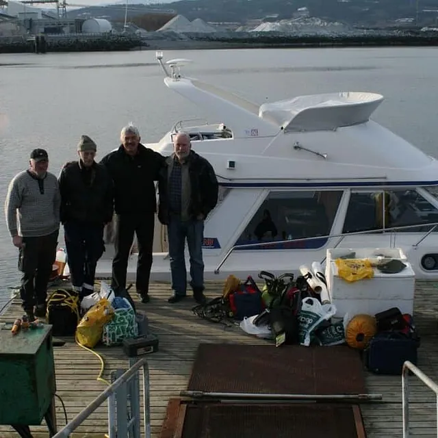 Fire menn poserer foran cabincruiser ved kai med utstyr på bryggen.
