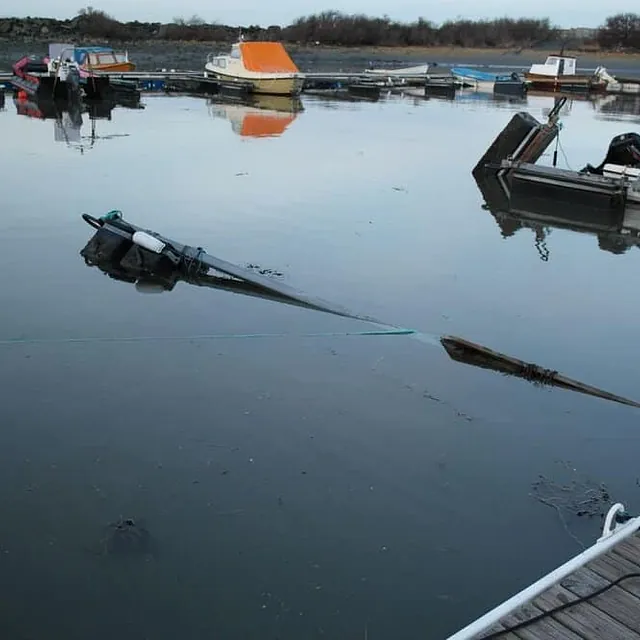 Delvis nedsunket båt ligger ved brygge i stille havnebasseng.